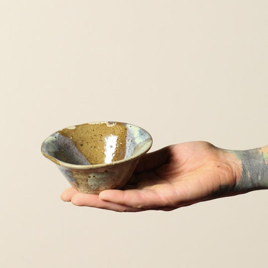 Hand holding a ceramic bowl with a textured surface on a beige background
