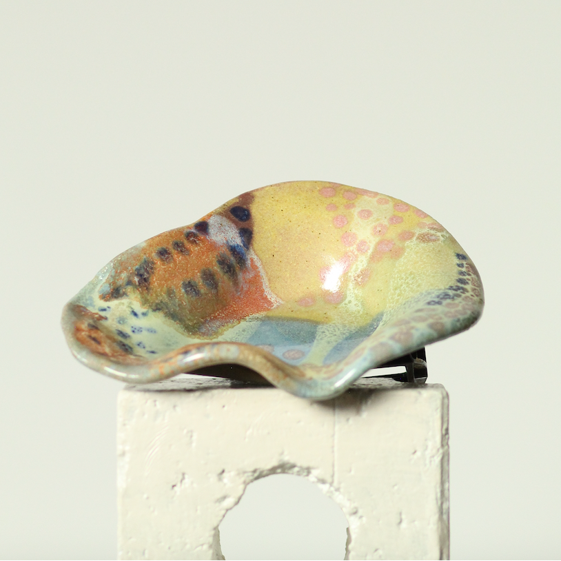 Colorful ceramic shell on a white pedestal against a light beige background