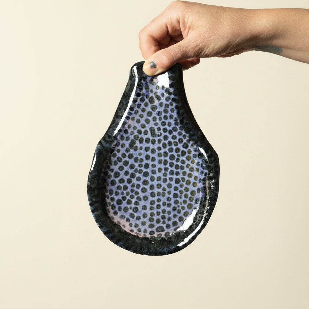 Hand holding a black ceramic spoon holder with gray speckles against a beige background