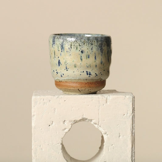 Ceramic espresso cup with speckled design on a concrete block against a beige background