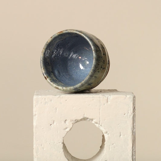 Blue ceramic espresso cup on a textured white platform against a beige background