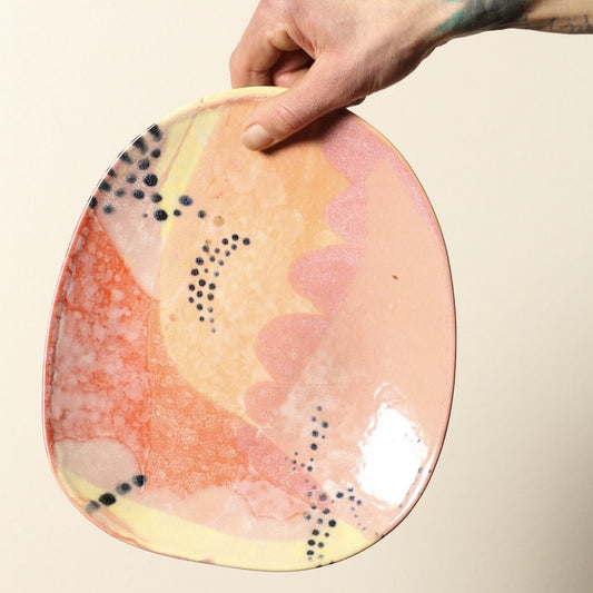 Hand holding a ceramic plate with abstract design on a beige background