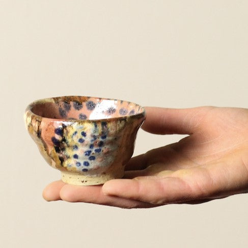 Hand holding a small ceramic bowl with speckled design on a beige background