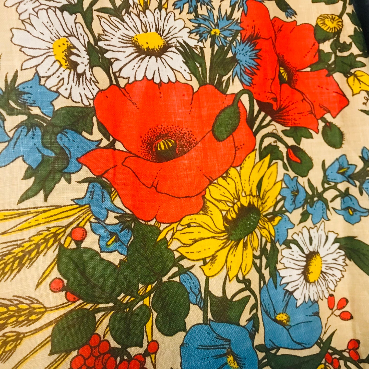 A close-up of a vintage floral fabric print featuring red poppies, yellow sunflowers, white daisies, blue flowers, green leaves, and wheat stalks on a cream-colored background.