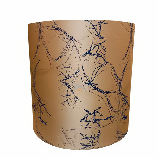 A cylindrical drum lampshade with a warm tan background and a black sketch-like abstract line pattern, shown against a plain off-white wall.