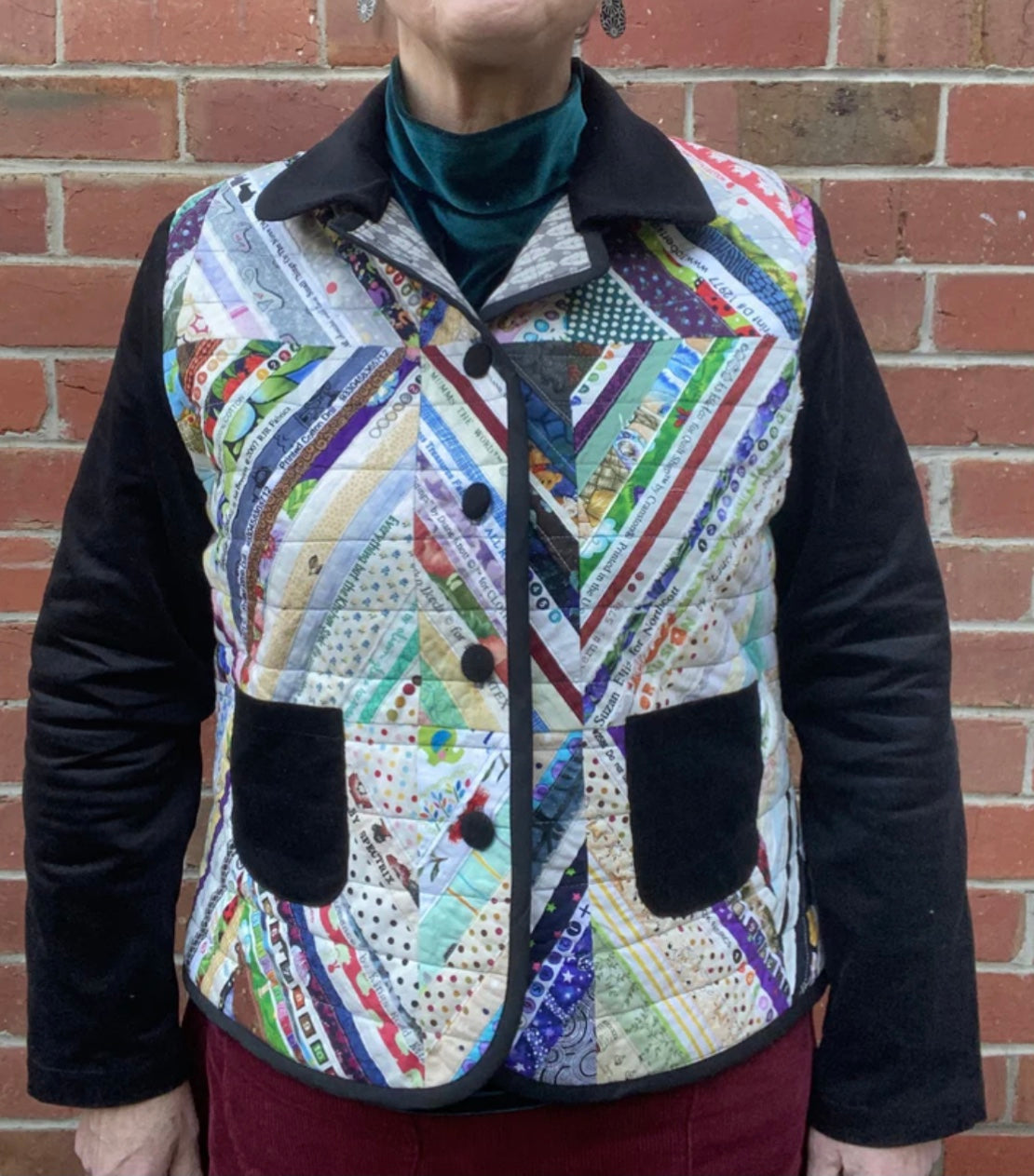 Person wearing a colorful quilted jacket with a brick wall background