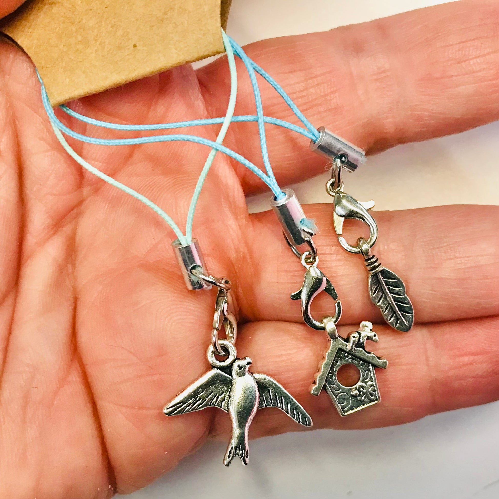 Silver charm bracelet with bird, house, and leaf charms held in a hand.