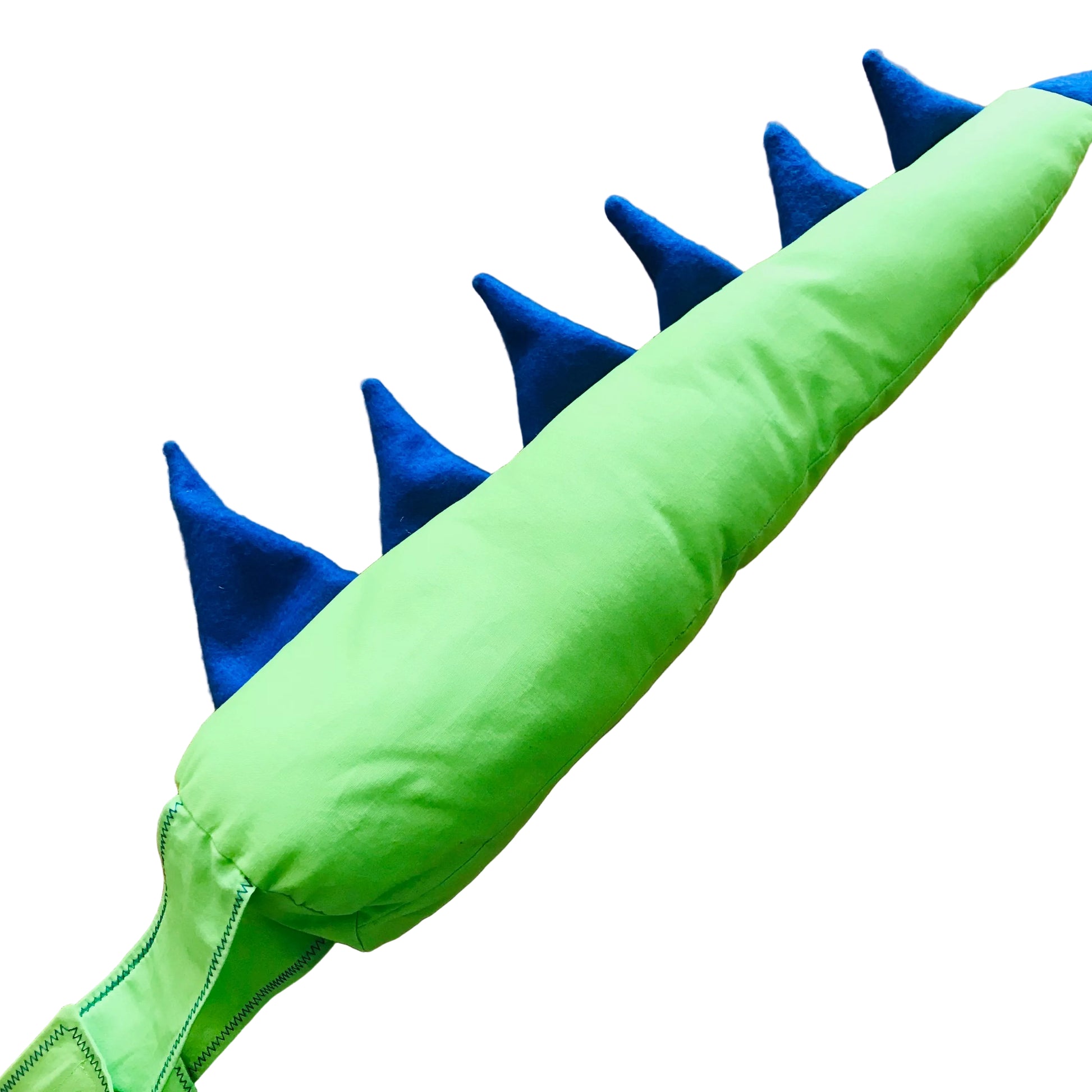 A close-up of a green dinosaur tail toy with blue felt spikes, laid diagonally on a light wood surface.