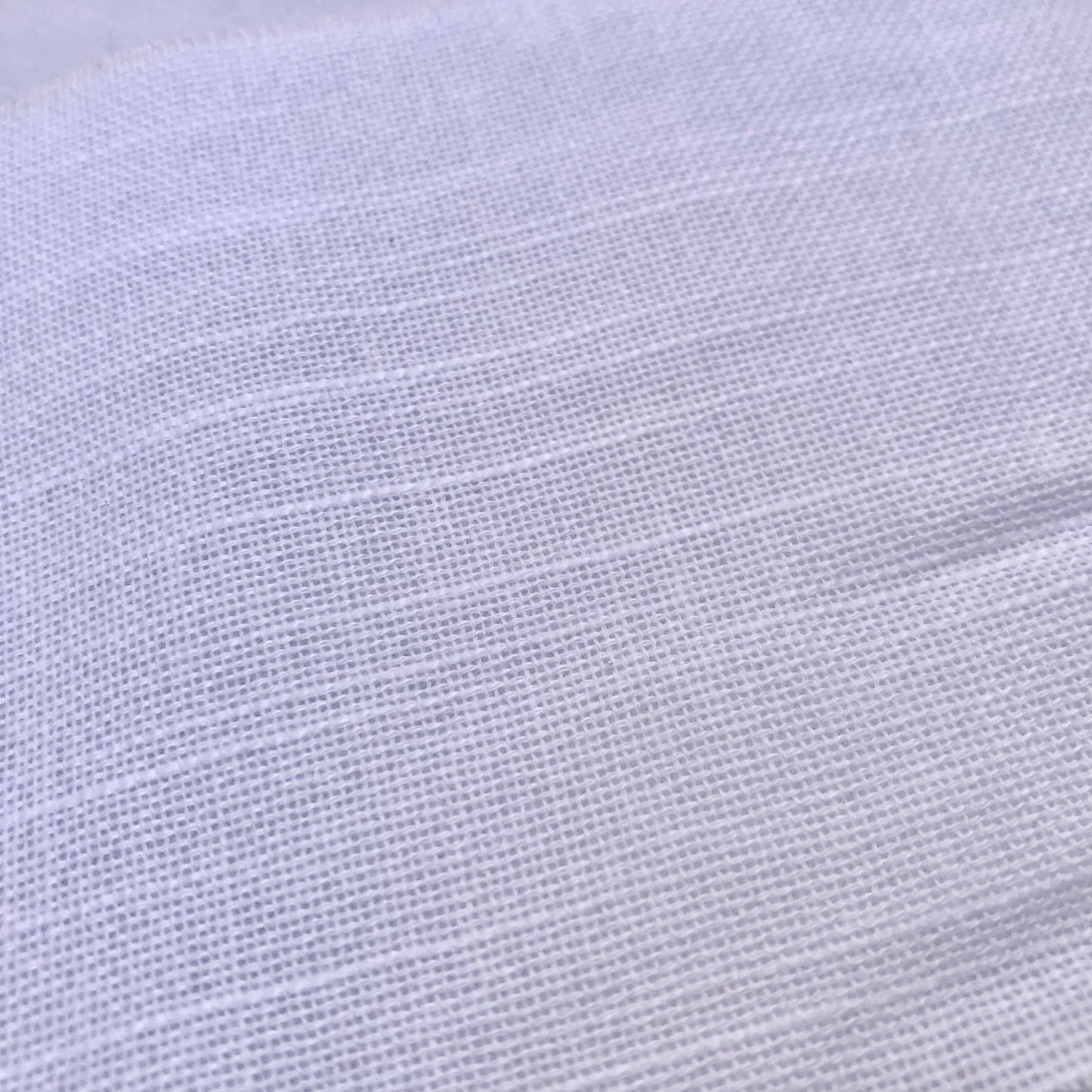 A close-up of white textured fabric with a fine woven pattern and soft horizontal folds.