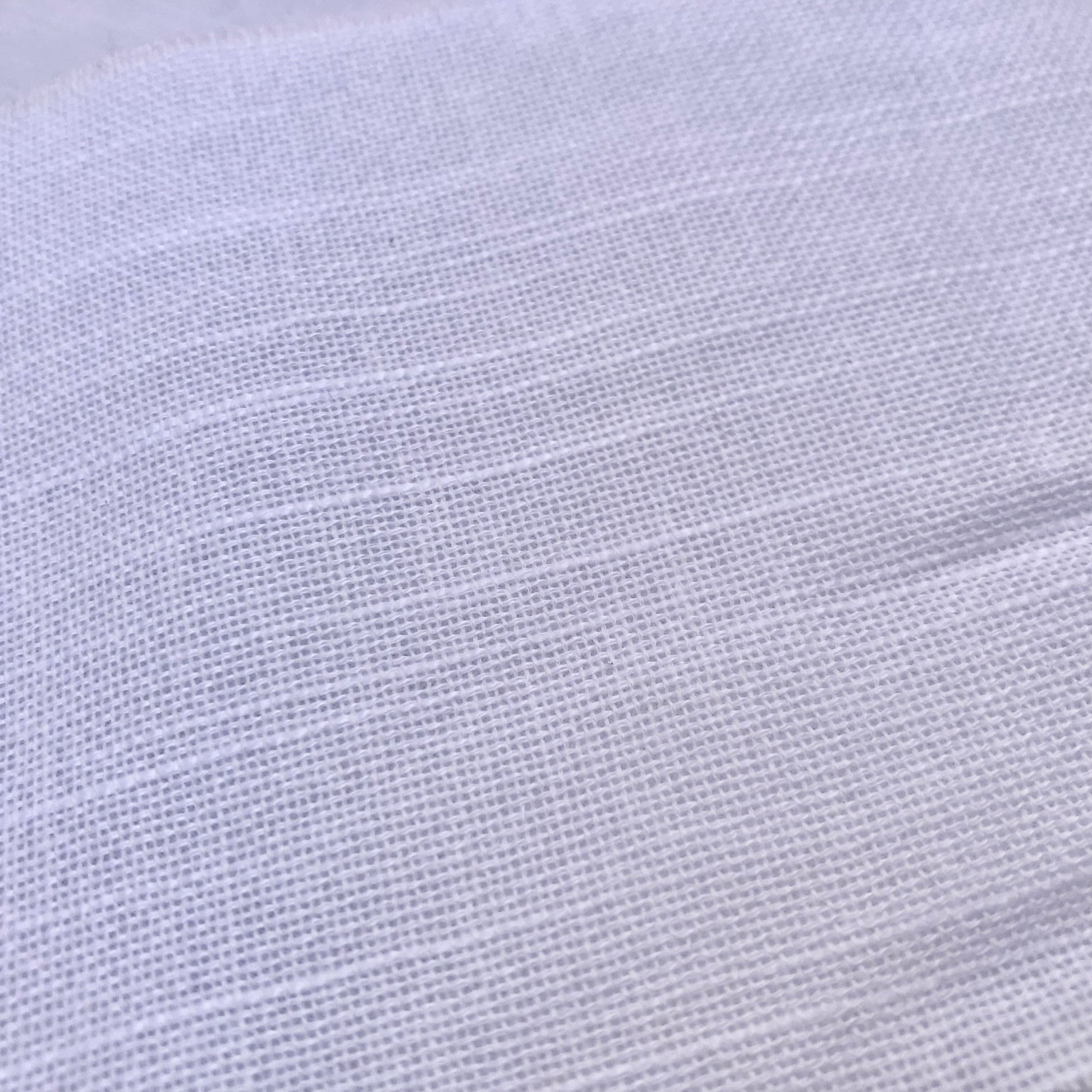 A close-up of white textured fabric with a fine woven pattern and soft horizontal folds.