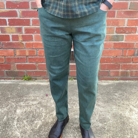 Person wearing green pants and a plaid shirt standing against a brick wall.