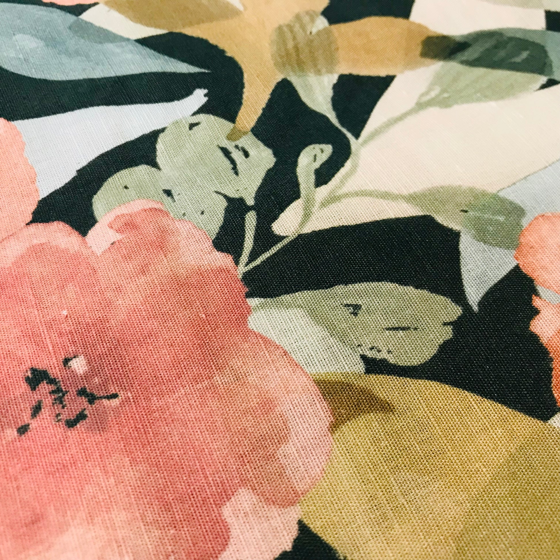 Close-up of a floral pattern with pink, green, and black colors on a textured fabric background.