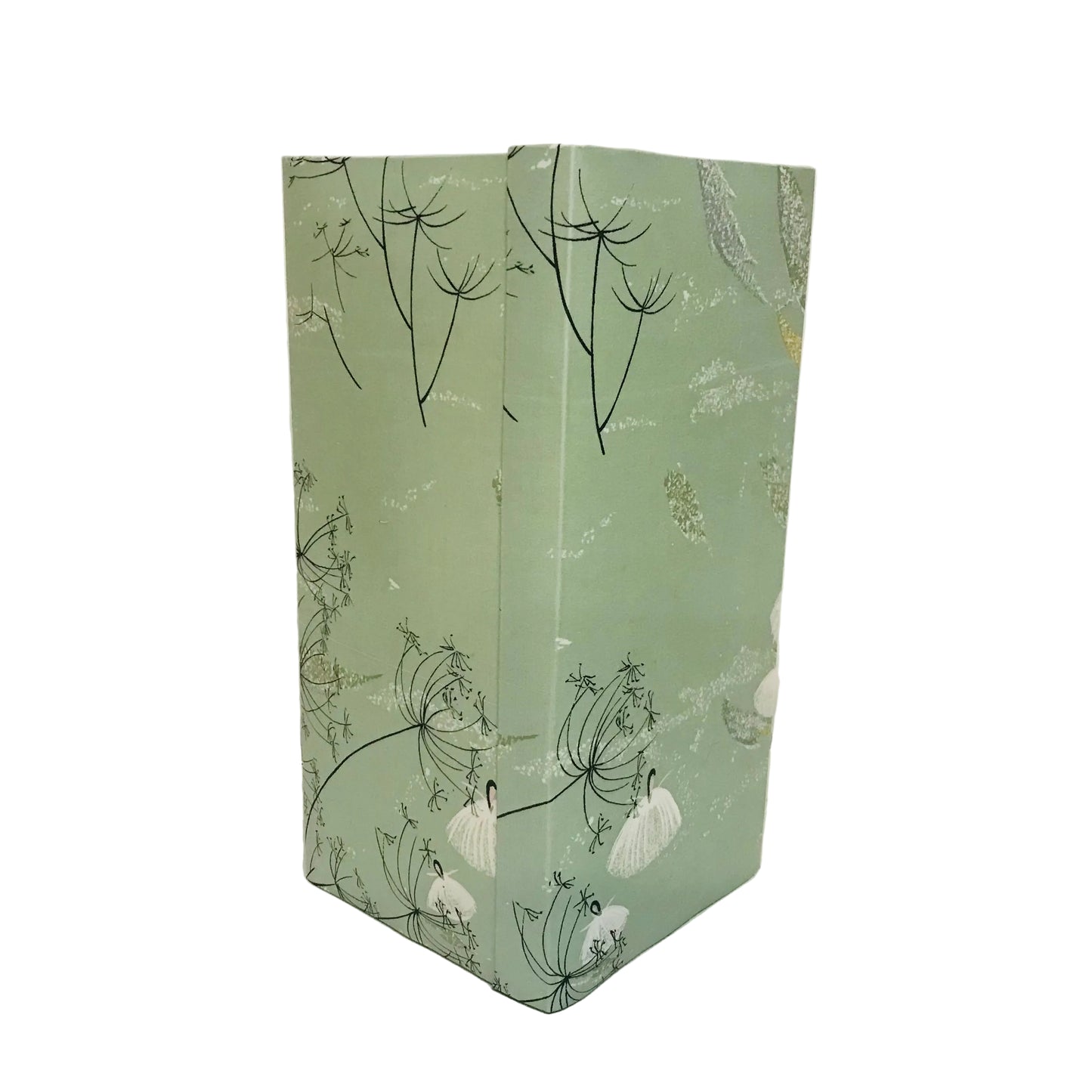A tal squared lampshade standing upright against a plain off-white wall and surface. It has a pale sage green background with a delicate black botanical line drawing and scattered white floral accents.