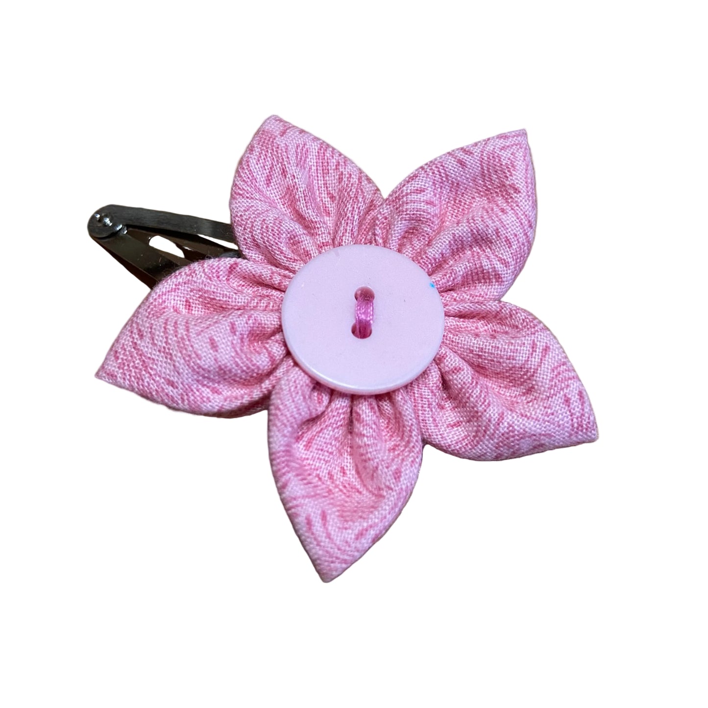Pink flower-shaped hair clip with a button center on a wooden surface