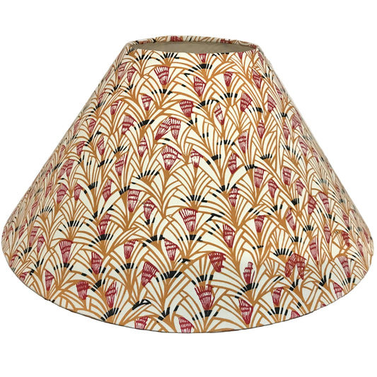 A fabric lampshade with a repeating Art Deco fan pattern in terracotta red, mustard yellow, and black on a cream background, photographed indoors against a plain light wall.