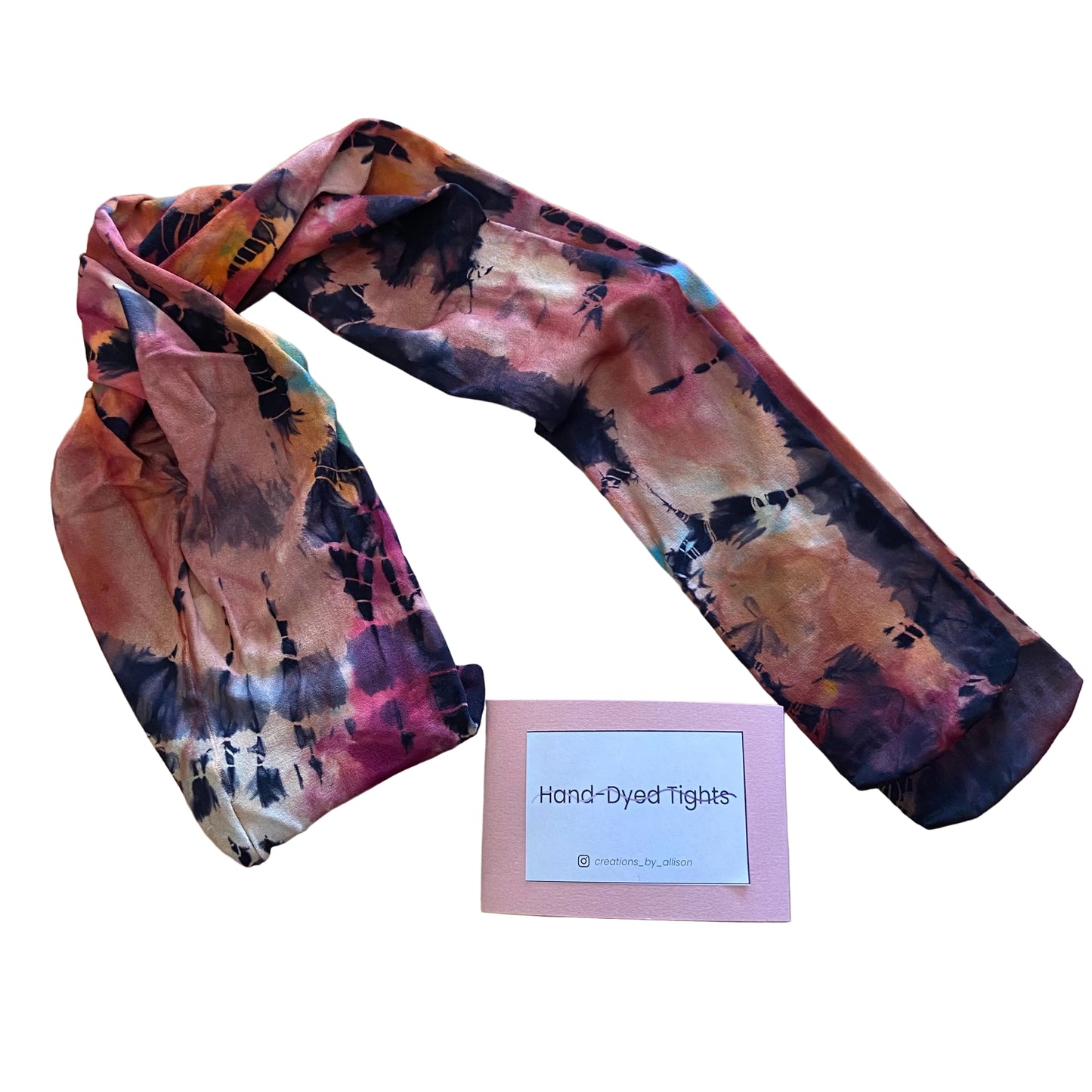Hand-dyed tights with a tie-dye pattern on a wooden surface, accompanied by a card labeled 'Hand-Dyed Tights'.