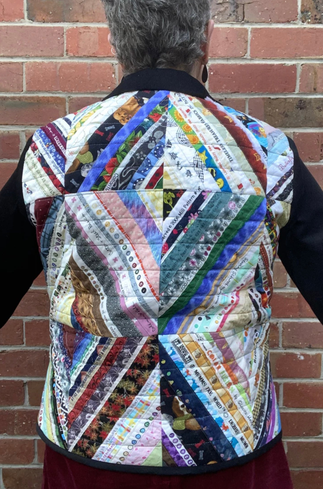 Person wearing a colorful quilted jacket against a brick wall.