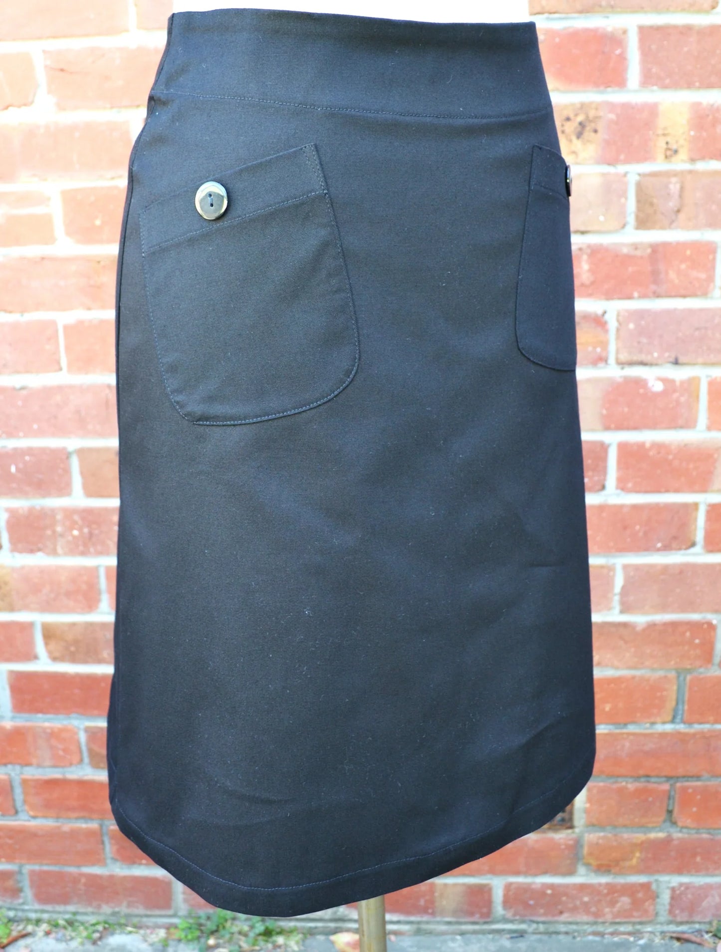 black skirt with a button on a mannequin against a brick wall.