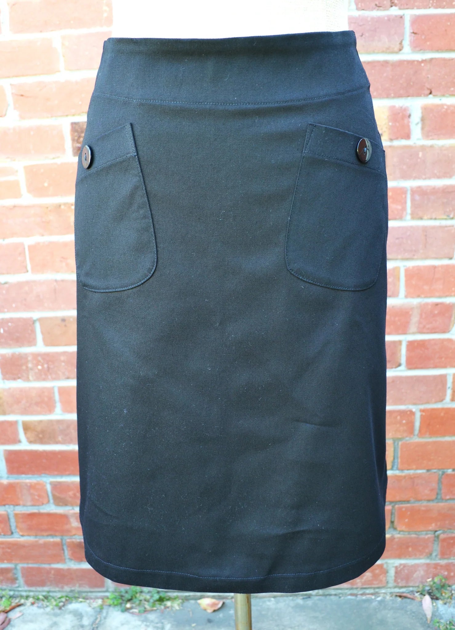 Black skirt with button details on a mannequin against a brick wall.