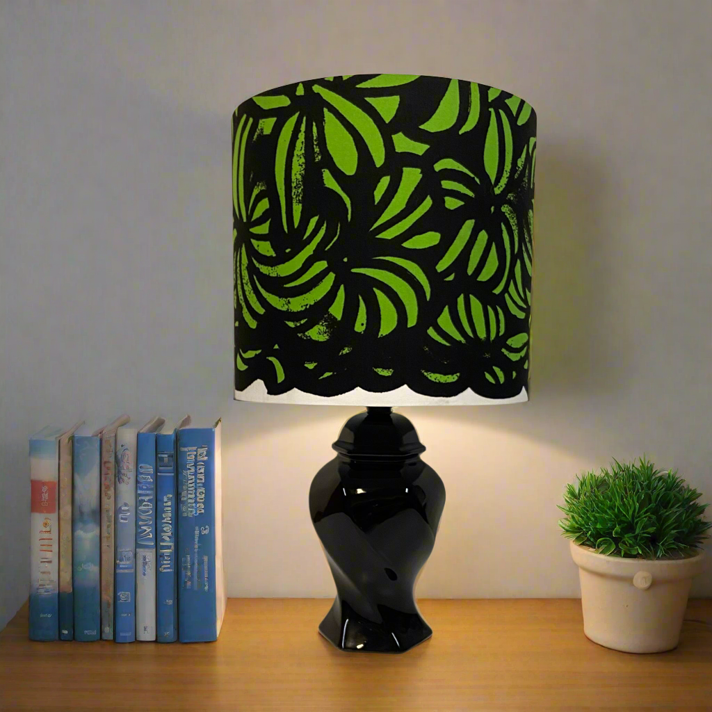 black ceramic, mid century table lamp with a lime green & black Marimekko shade place displayed on a side table with books and a green plant.