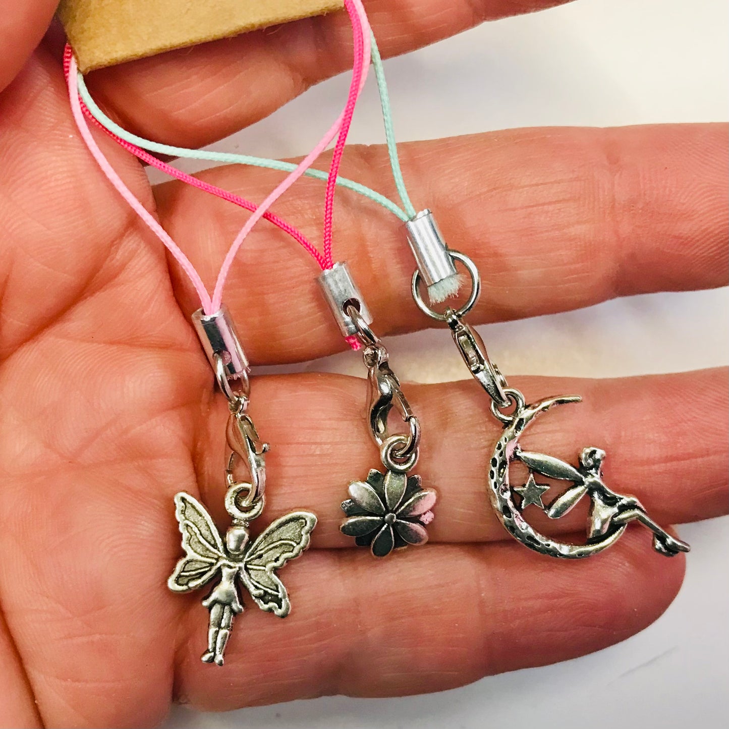 Three small silver charms on strings held in a hand