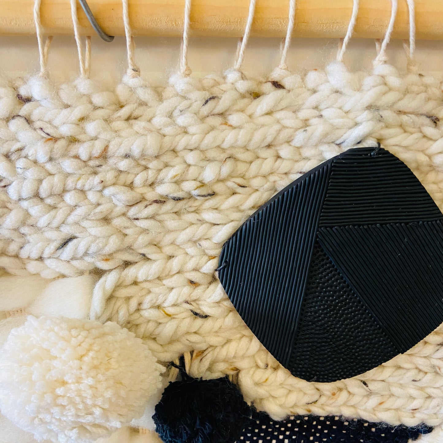Black woven coaster on a textured beige surface with yarn and a wooden tool.