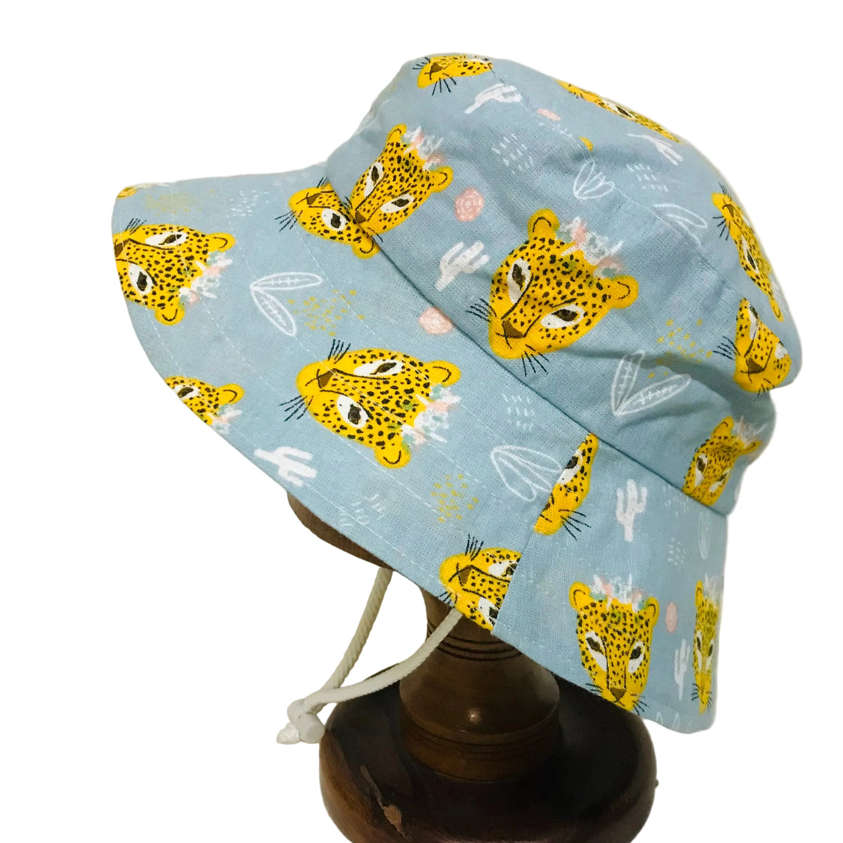 A light blue bucket hat with a yellow leopard print pattern, displayed on a wooden stand against a plain white background.