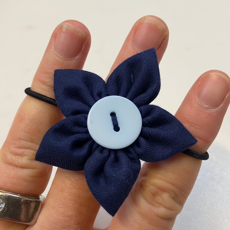 Navy blue fabric flower with a white button center on a finger against a plain background