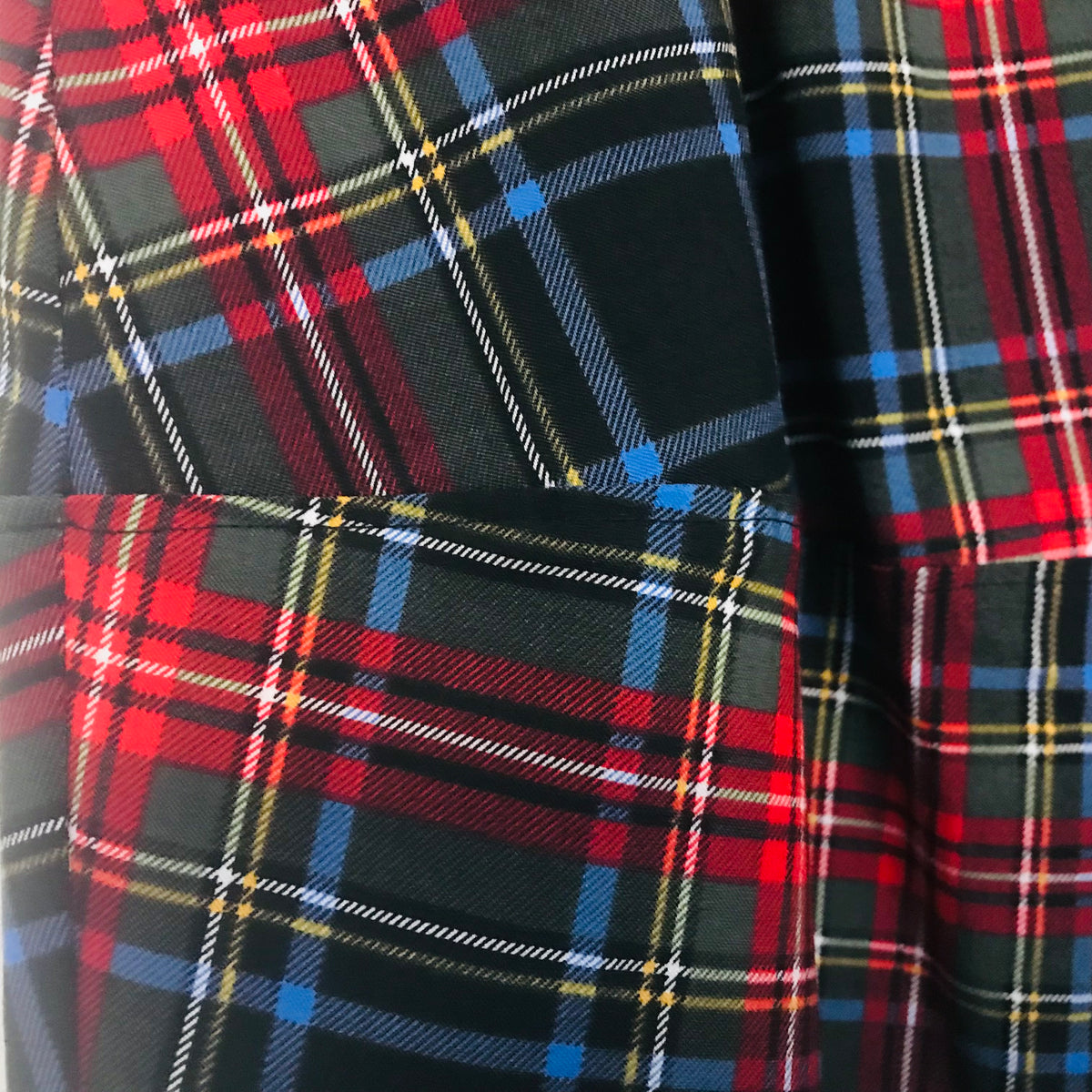 A close-up of a tartan plaid fabric with a black base and intersecting red, blue, yellow, and white stripes.