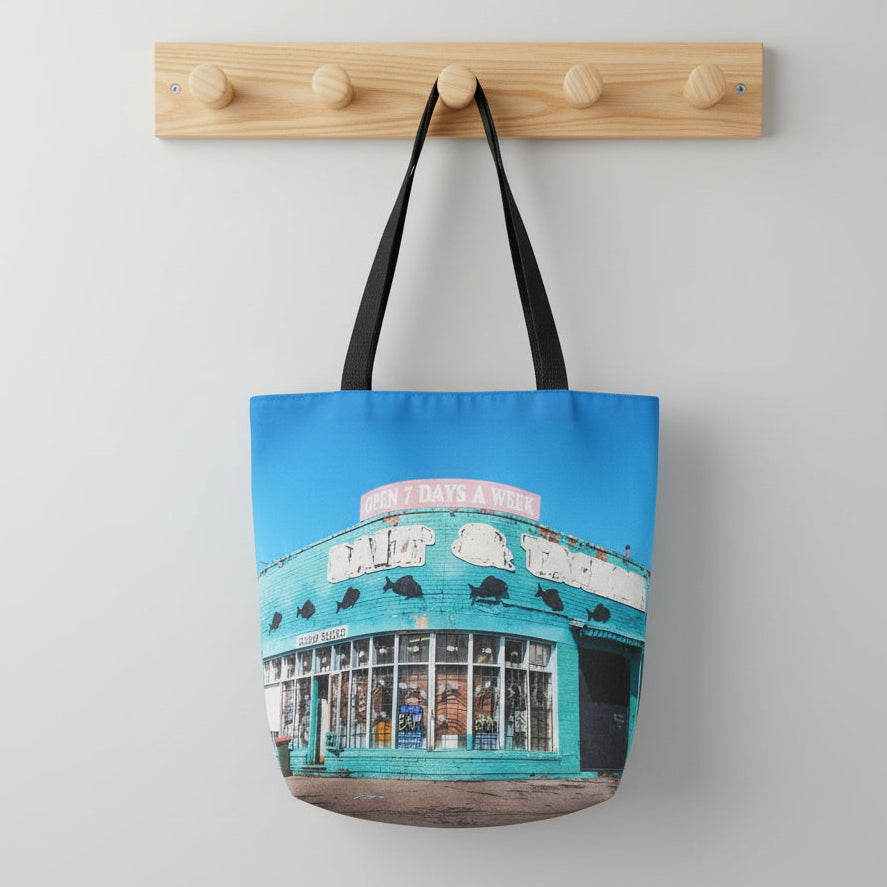 Tote bag with a the wiliamstown bait shop printed on it, hanging on a wooden hook against a light gray background.
