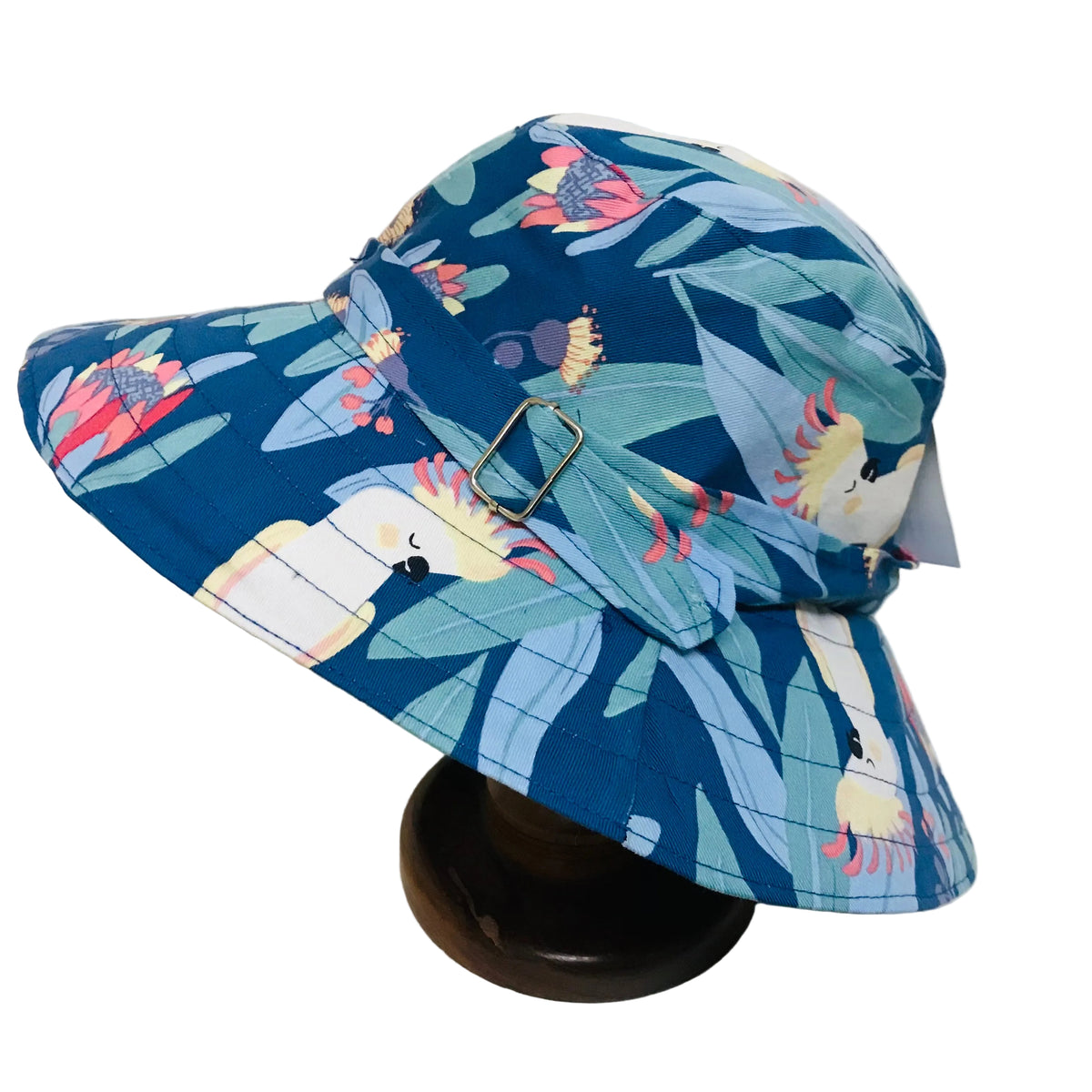 A wide-brimmed bucket hat with a blue tropical floral and bird print, displayed on a dark wooden stand against a white background.