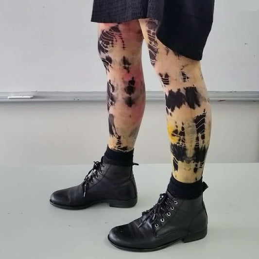 Person wearing black lace-up boots and colorful tie-dye leggings against a plain background