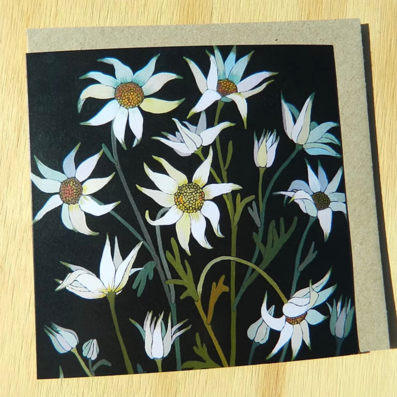greeting card with white flowers on a black background, placed on a wooden surface.