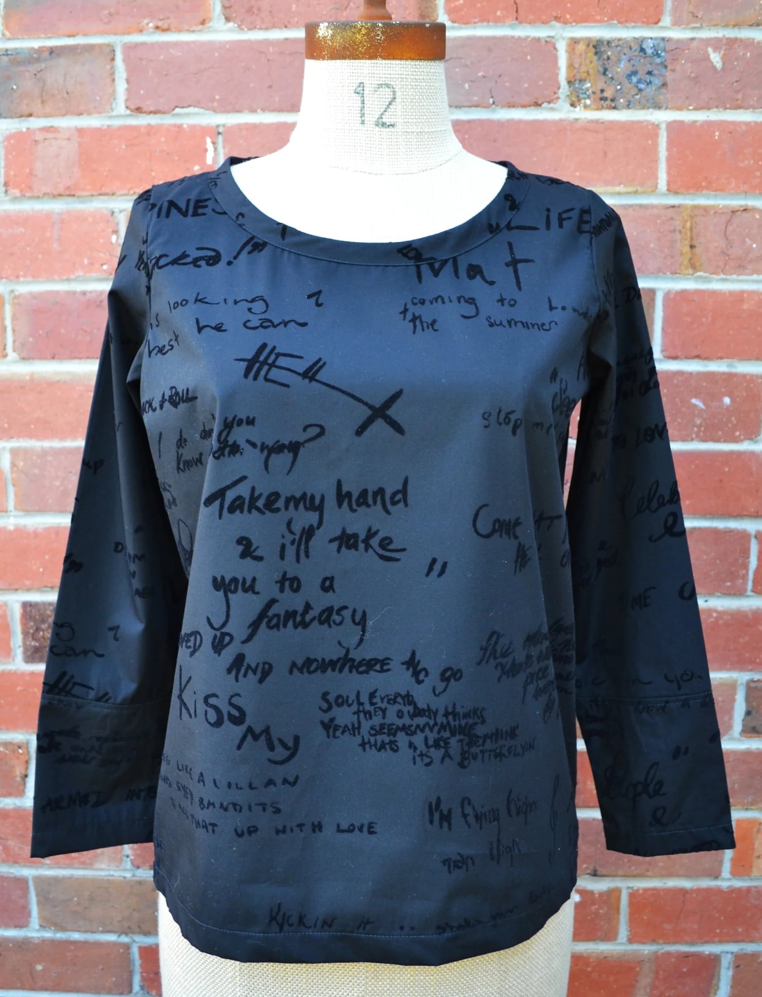 Black long-sleeve shirt with text on a mannequin against a brick wall.