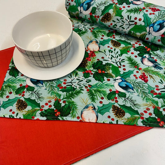 Christmas-themed placemats with birds and holly on a red surface