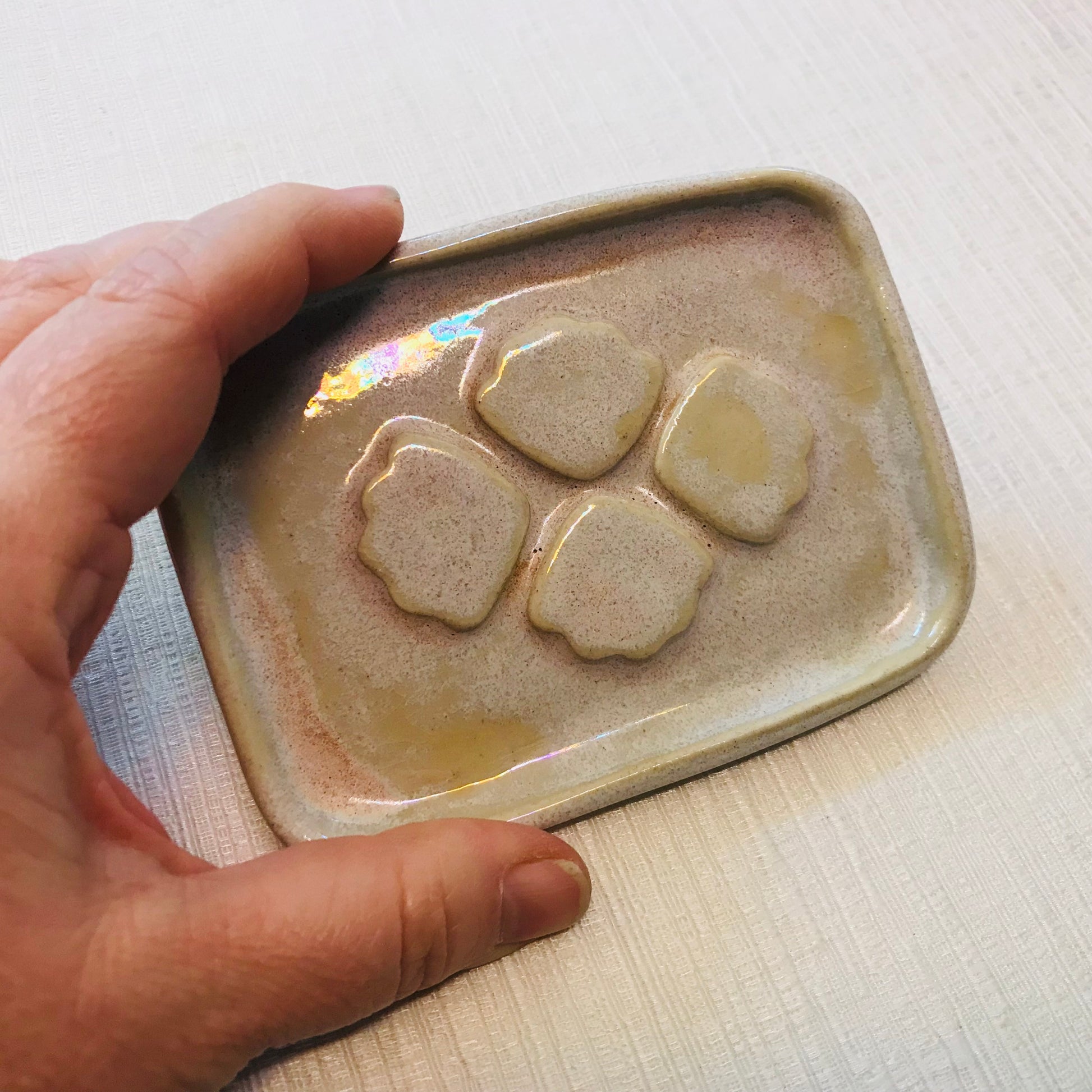Hand holding a ceramic soap dish with four stone-like shapes on a light background