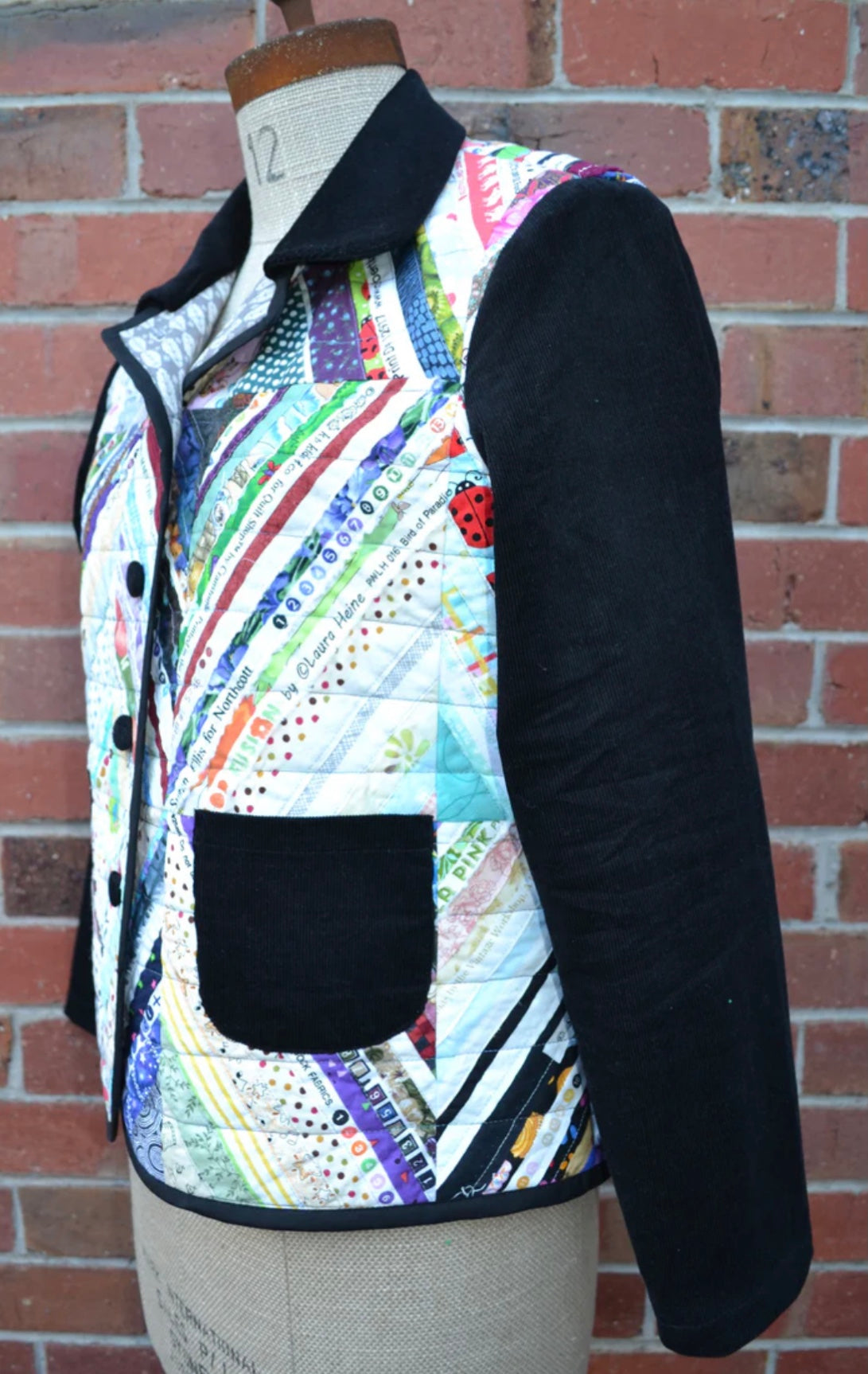 Colorful quilted jacket on a mannequin against a brick wall.