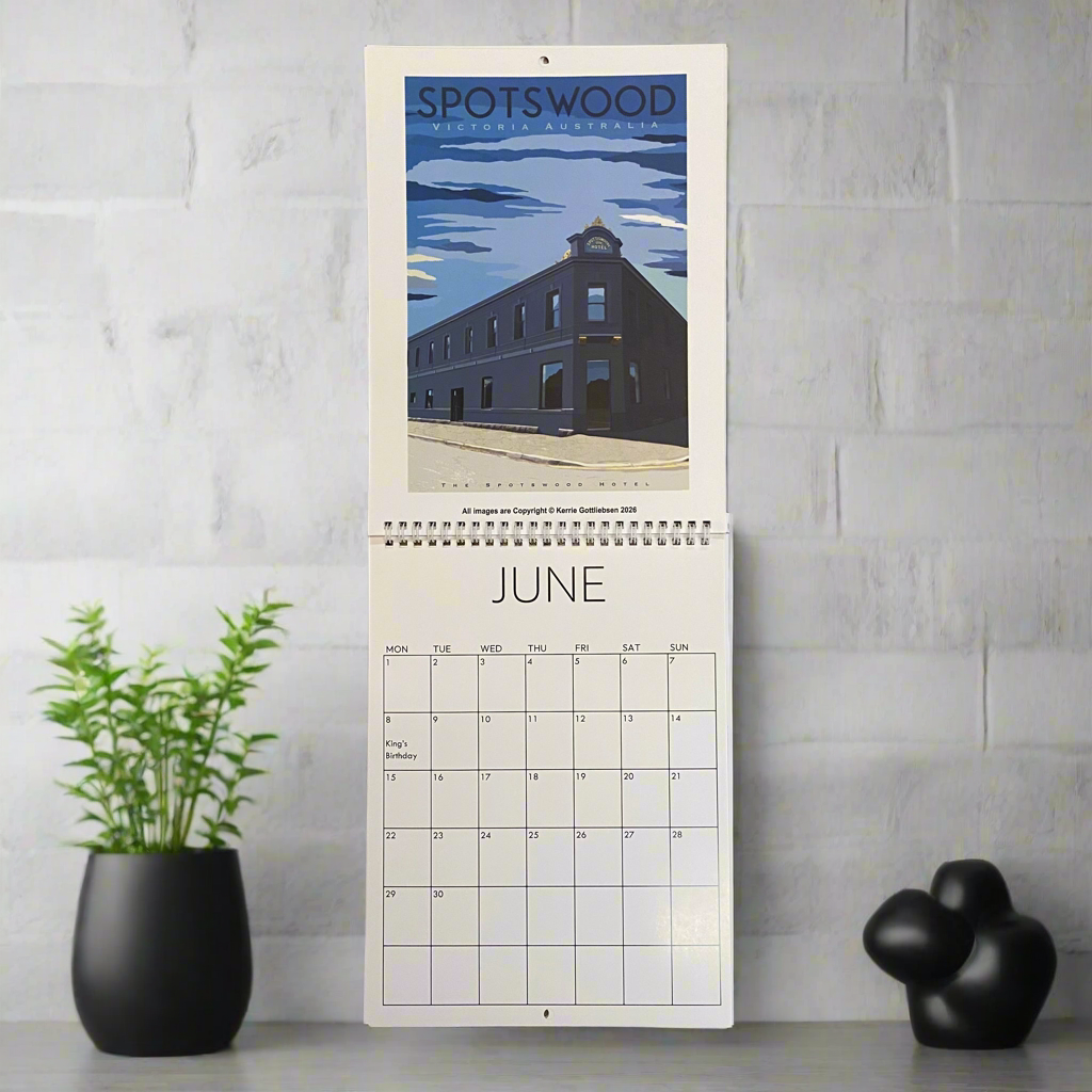 Calendar with a scenic design of a building and water body, placed on a light gray surface with decorative items.
