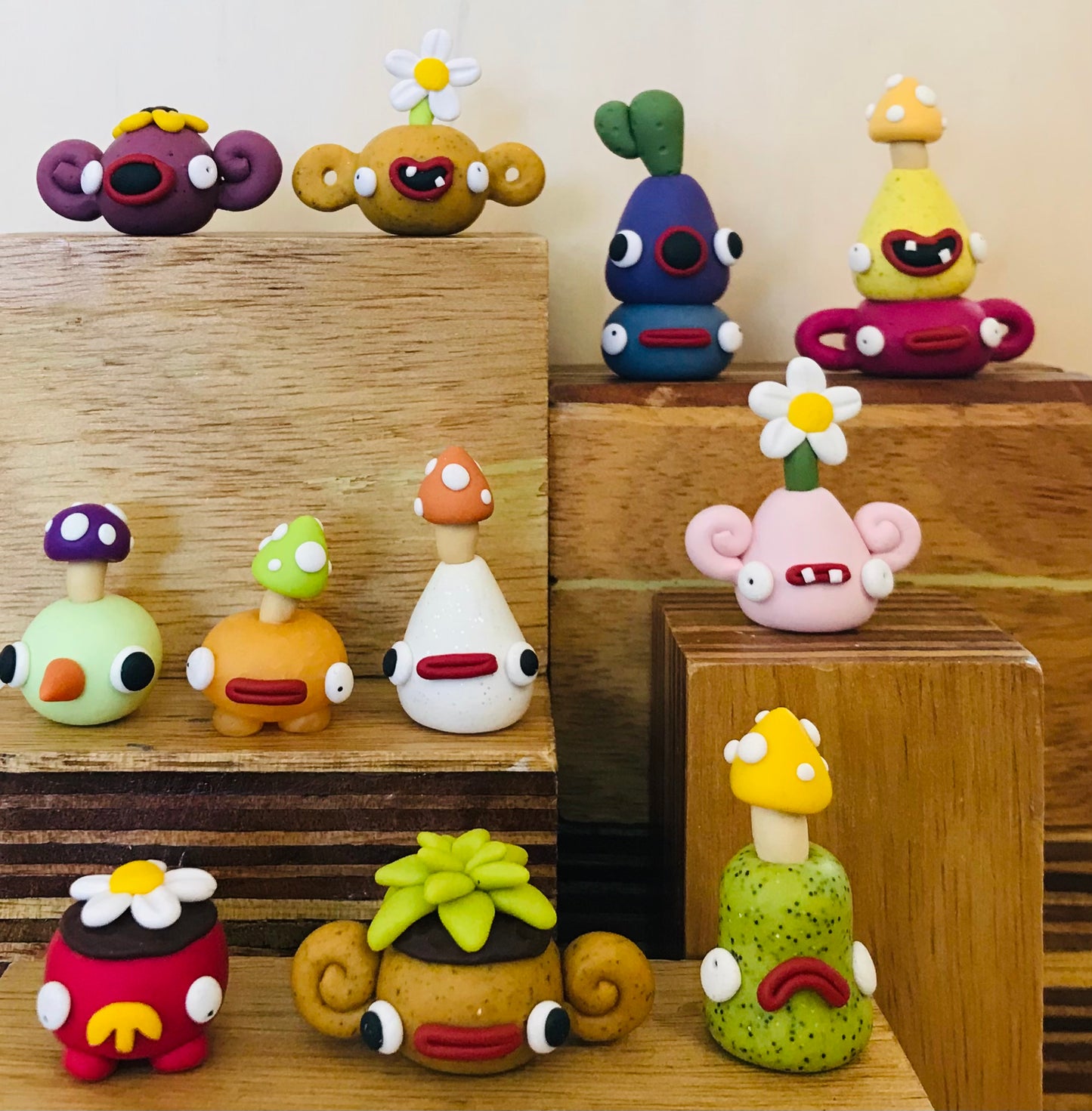A collection of colorful handmade clay figurines shaped like stylized mushrooms and cartoon characters, displayed on wooden blocks against a neutral background.