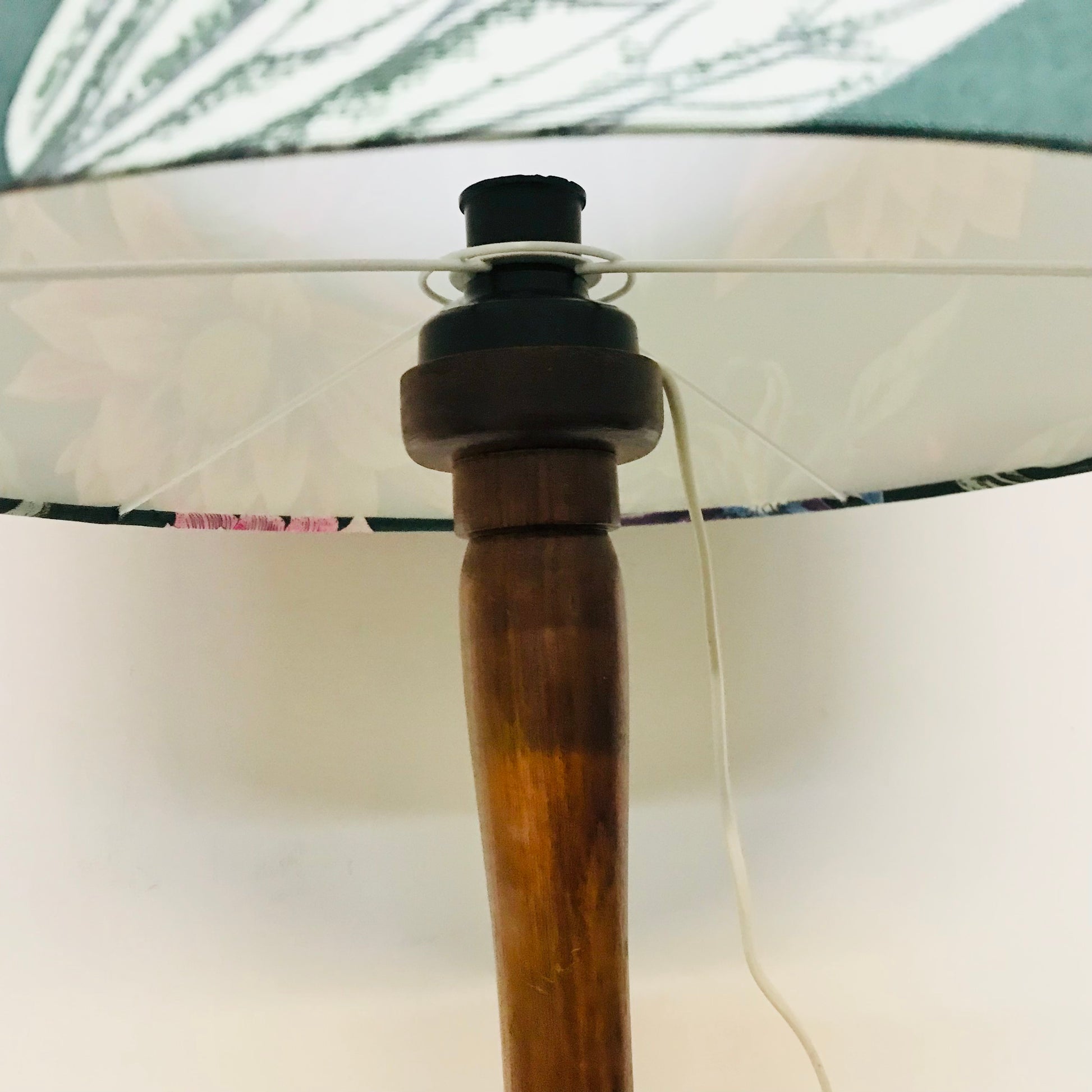 Close-up of a wooden lamp post and shade assembly, showing a patterned white fabric shade with green and pink botanical details, a black top cap, and a white cord.