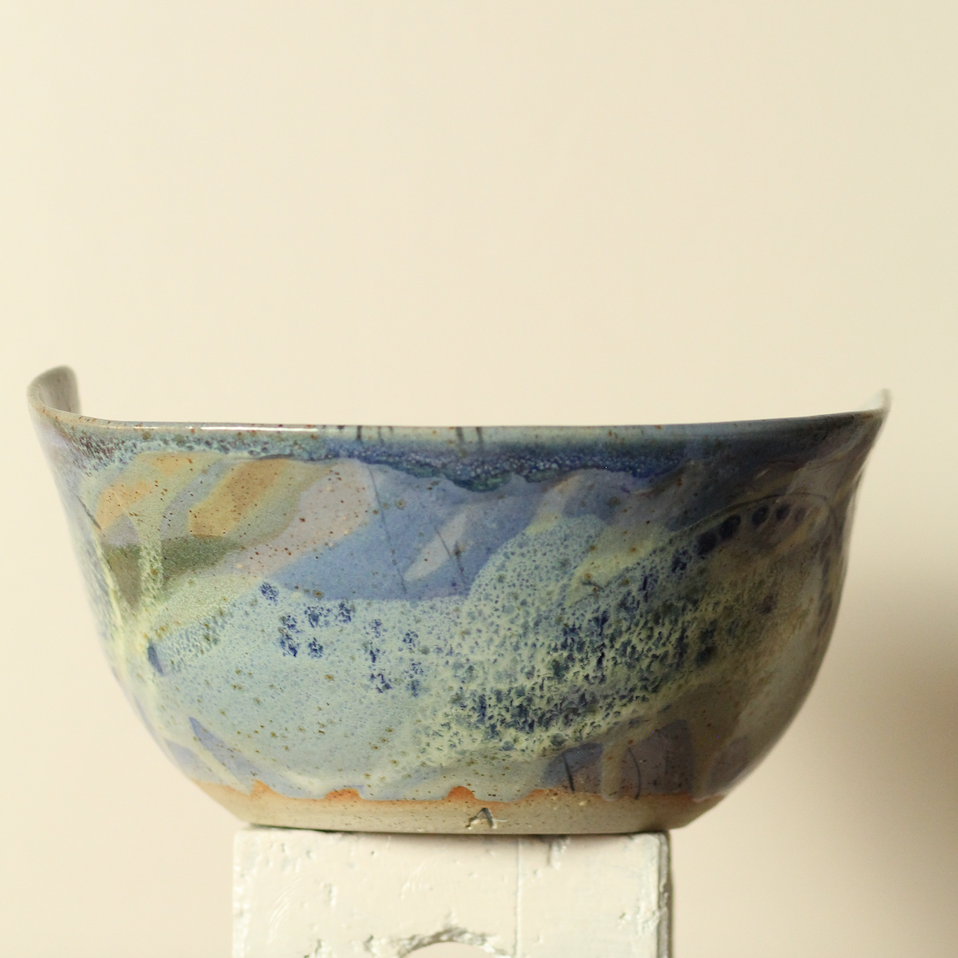 Handmade ceramic bowl with abstract multicolor design on a neutral background
