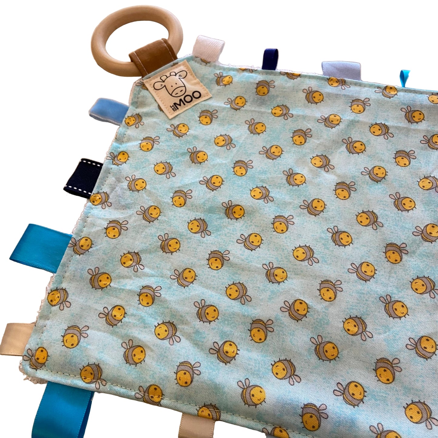 Fabric baby taggie toy with a bee pattern and wooden ring on a beige background