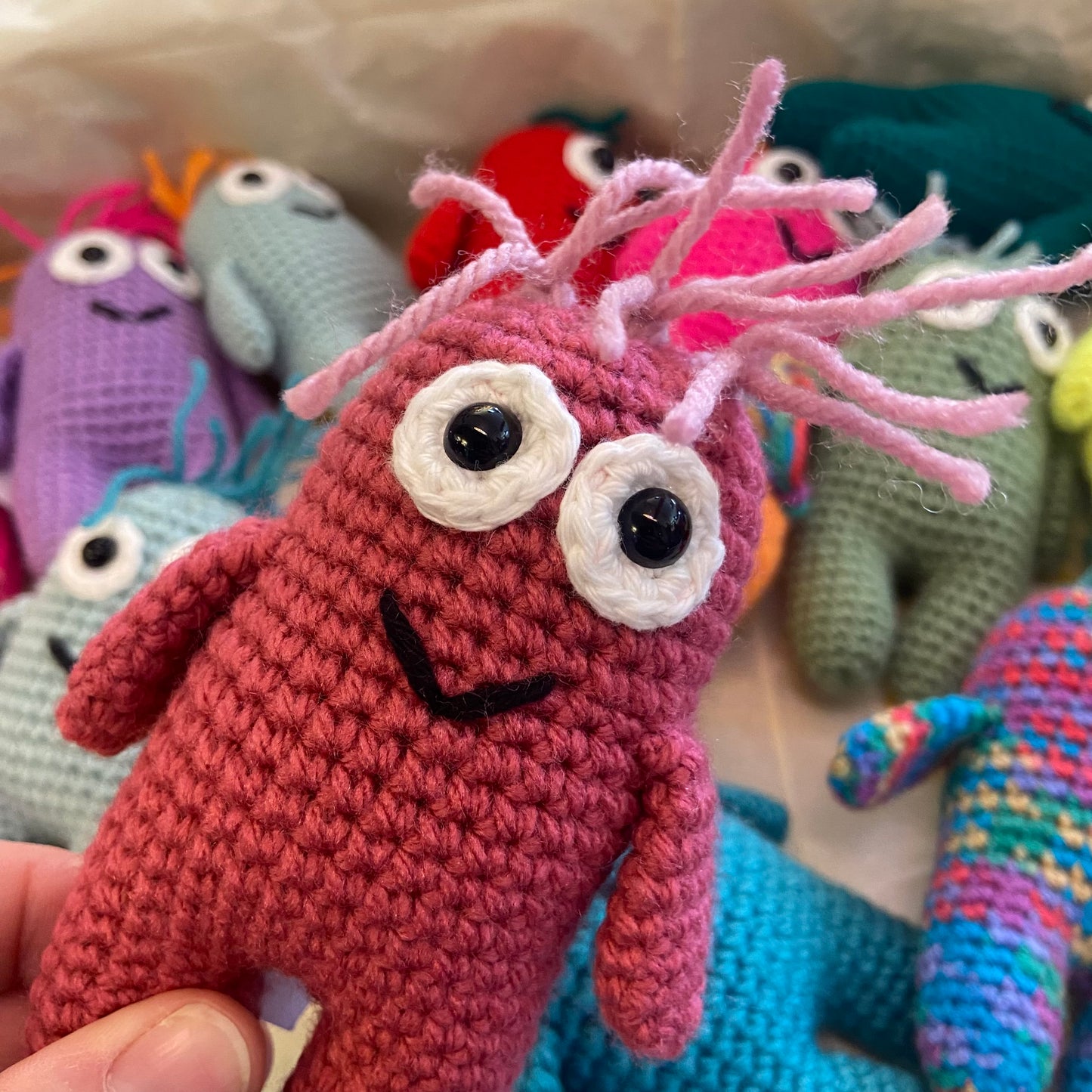 Handmade crochet toy with pink body and white face held in front of other colorful toys.