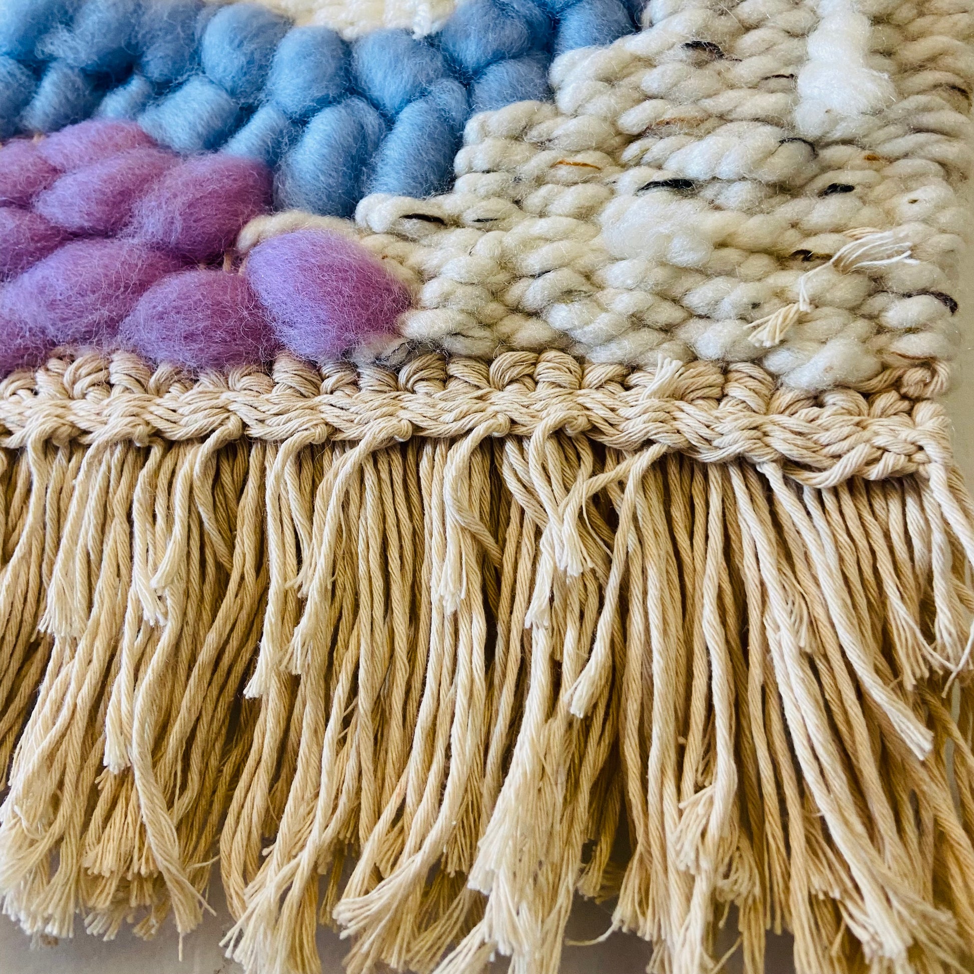Close-up of a textured fabric with colorful pom-poms and fringes.