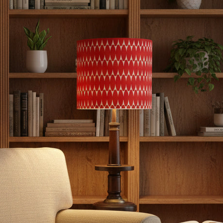 A table lamp with a red and white geometric patterned drum shade and a dark brown wooden base, shown standing on a white surface against an off-white wall.