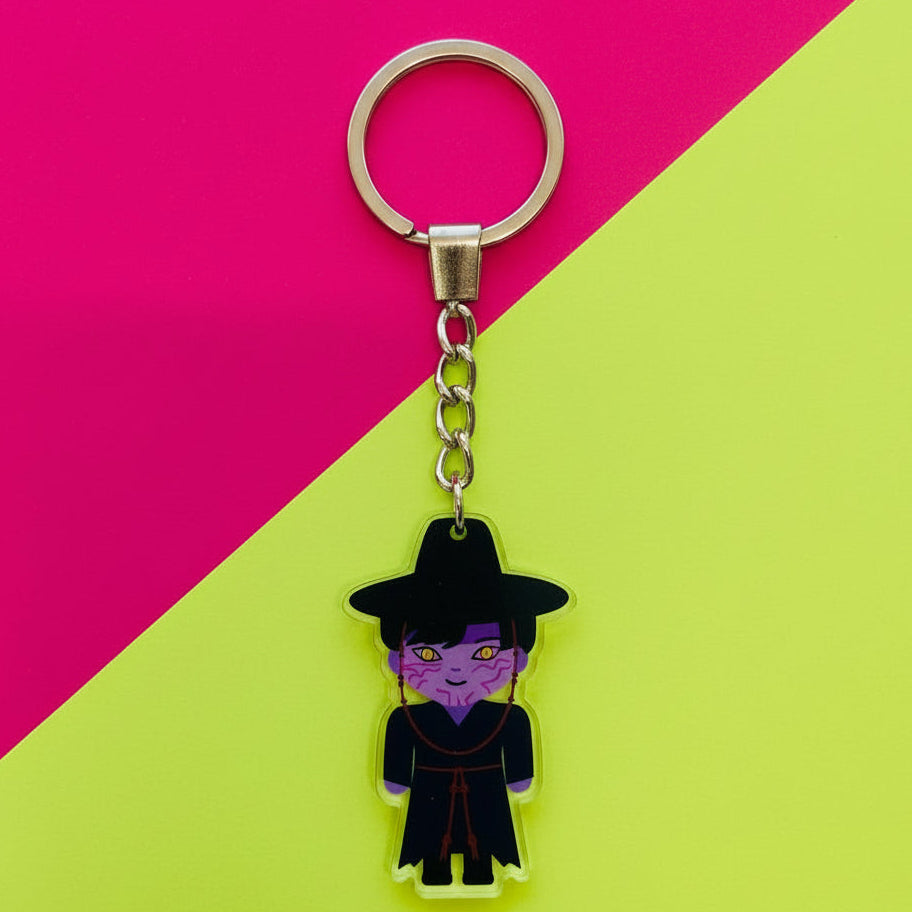 Keychain with a character in a black outfit and hat on a beige background