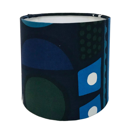 A cylindrical fabric lampshade featuring a mid-century modern abstract geometric pattern in navy, blue, green, and white, photographed against a plain white background.