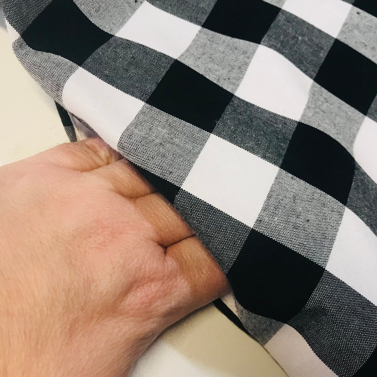 A close-up of a hand lifting the pocket of black and white buffalo plaid fabric to show its texture and weight.