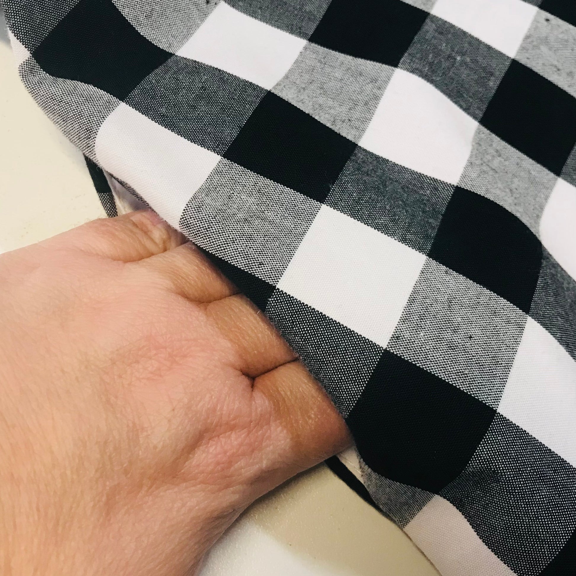 A close-up of a hand lifting the pocket of black and white buffalo plaid fabric to show its texture and weight.