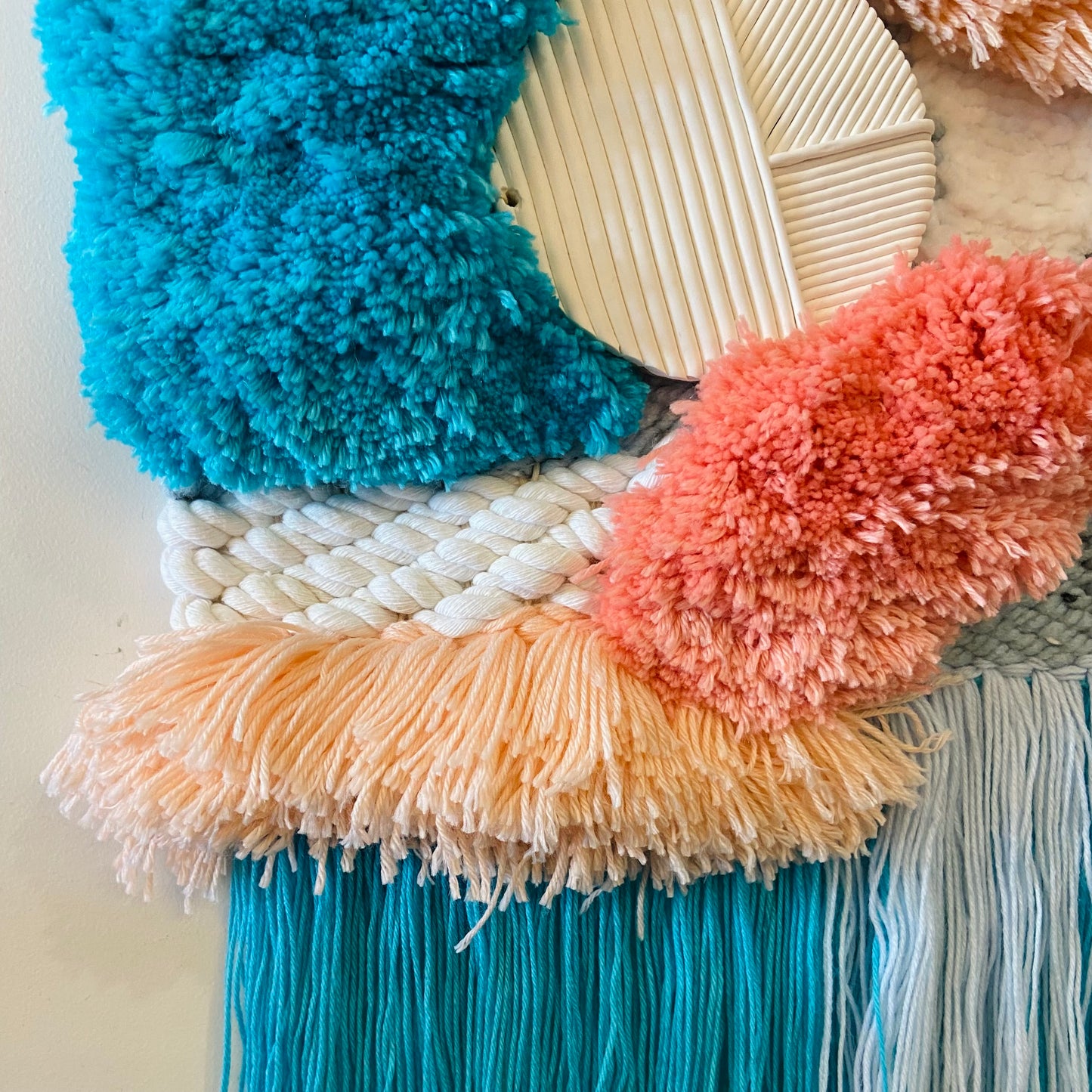 Woven wall art with colorful yarn fringe on a neutral background